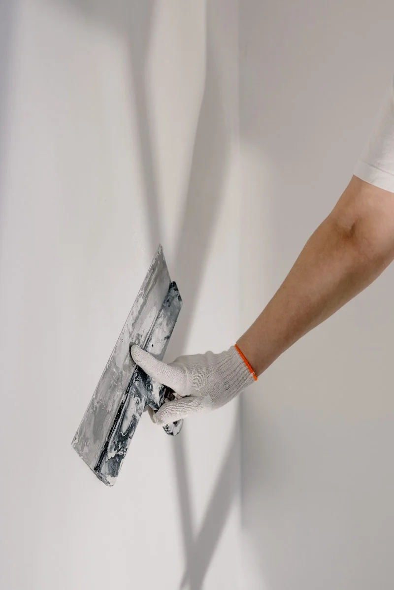 person using a tools to even out wall plaster