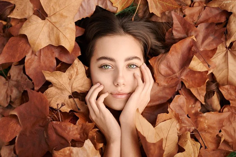 woman laying in between fall leaves