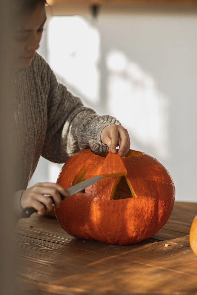 woman removing a piece from carved pumpkin