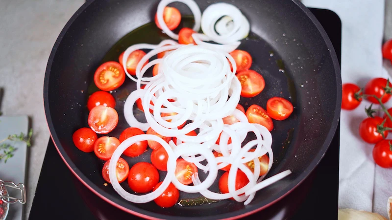 halved cherry tomatoes and onions in pan