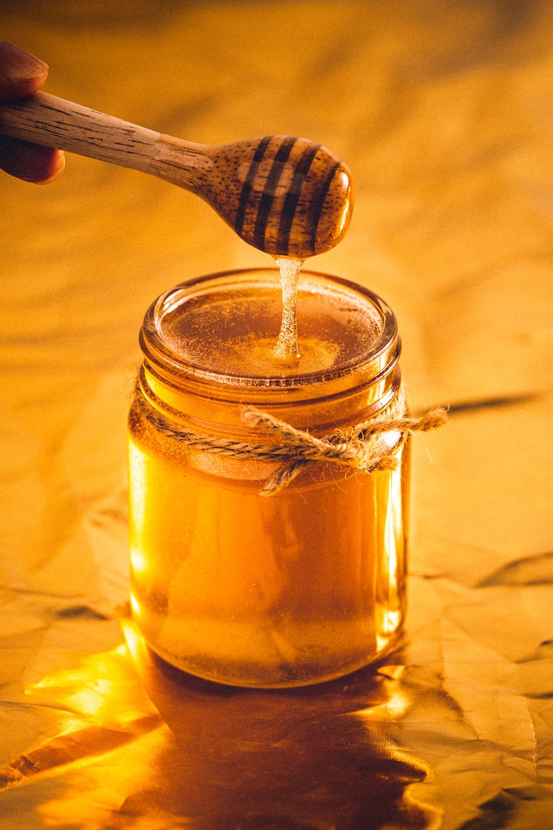 honey spoon being dipped in honey on golden background