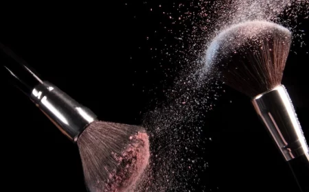 makeup brushes colliding with powder on them on black background