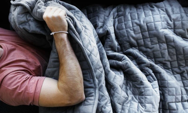 man sleeping with a gray heavy blanket