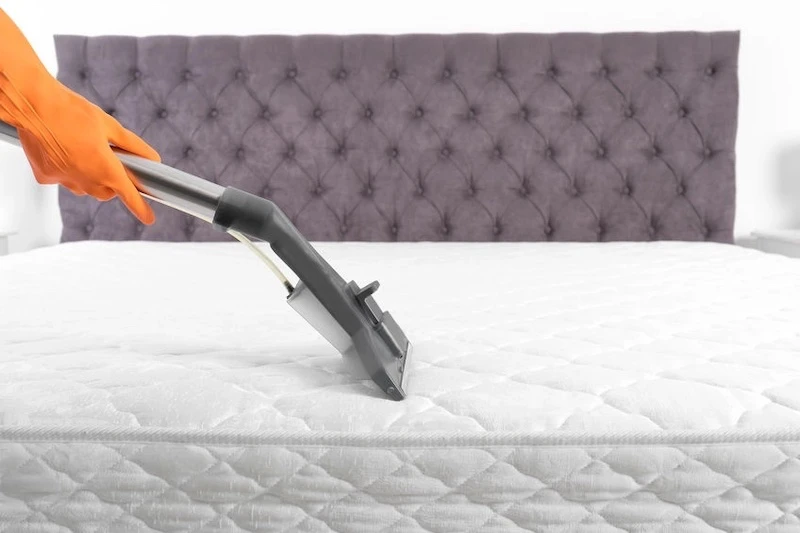 person vacuuming a white mattress