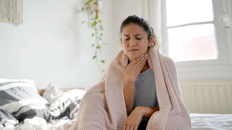 woman sitting in bed holding her throat
