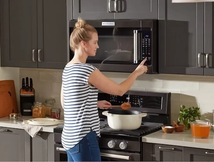 woman using built in microwave in black kitchen