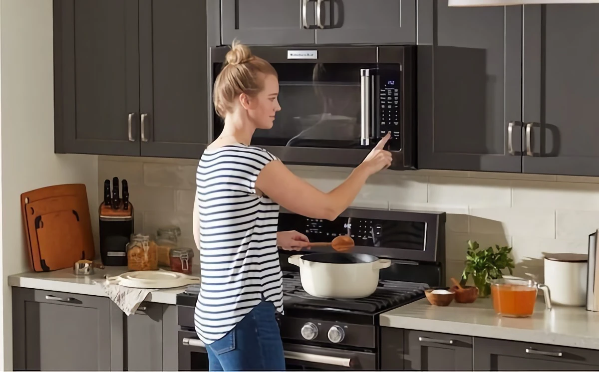 woman using built in microwave in black kitchen