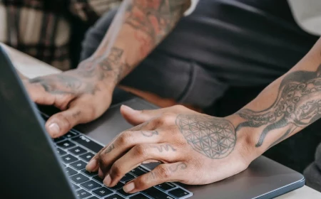 person with arm tattoos working on laptop