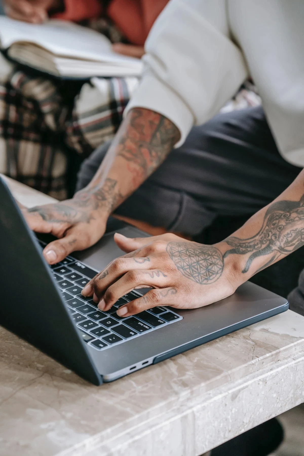 person with arm tattoos working on laptop