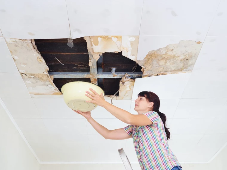 young woman collecting water in basin from ceiling. ceiling pane