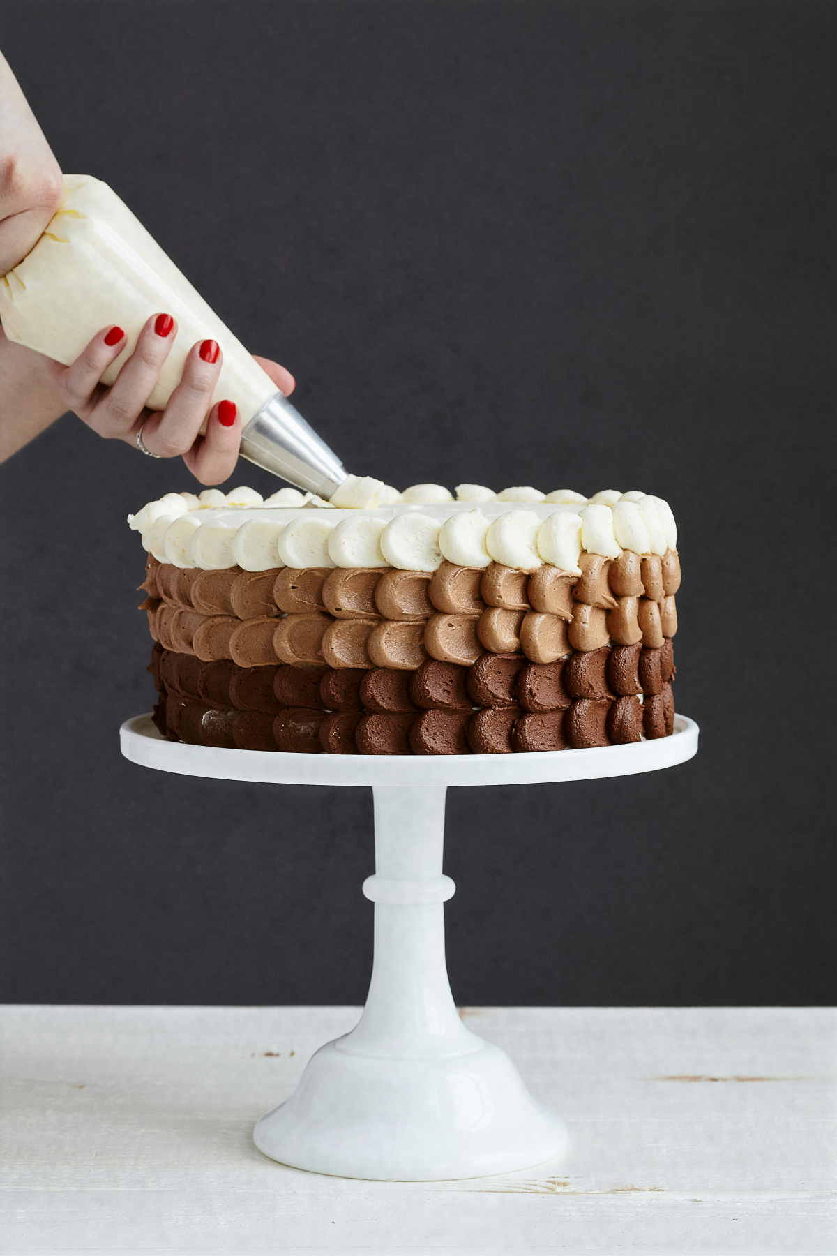 person piping a cake with white brown and dark brown icing